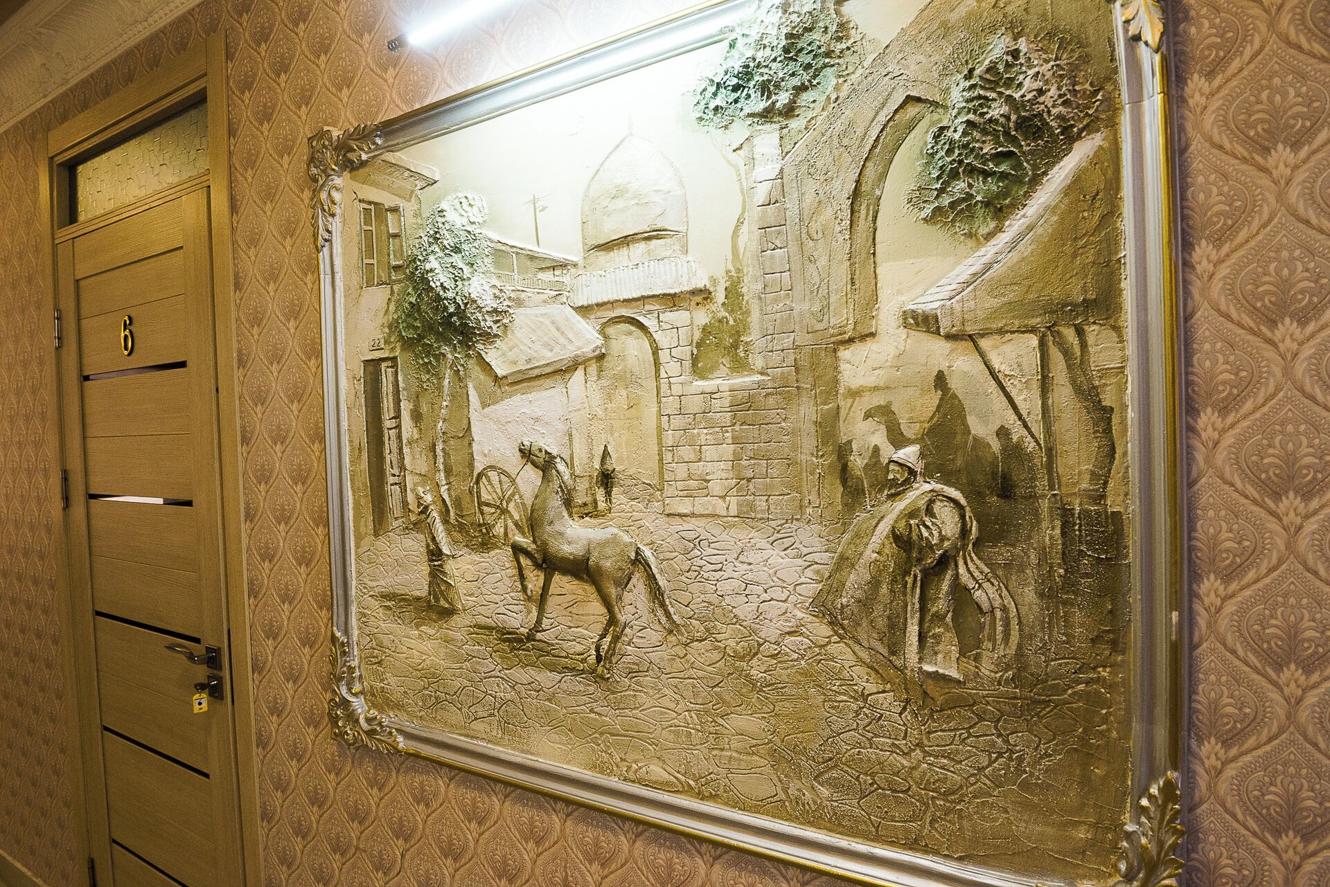 Quarto com uma grande pintura emoldurada retratando uma cena histórica, porta de madeira com número e papel de parede estampado.