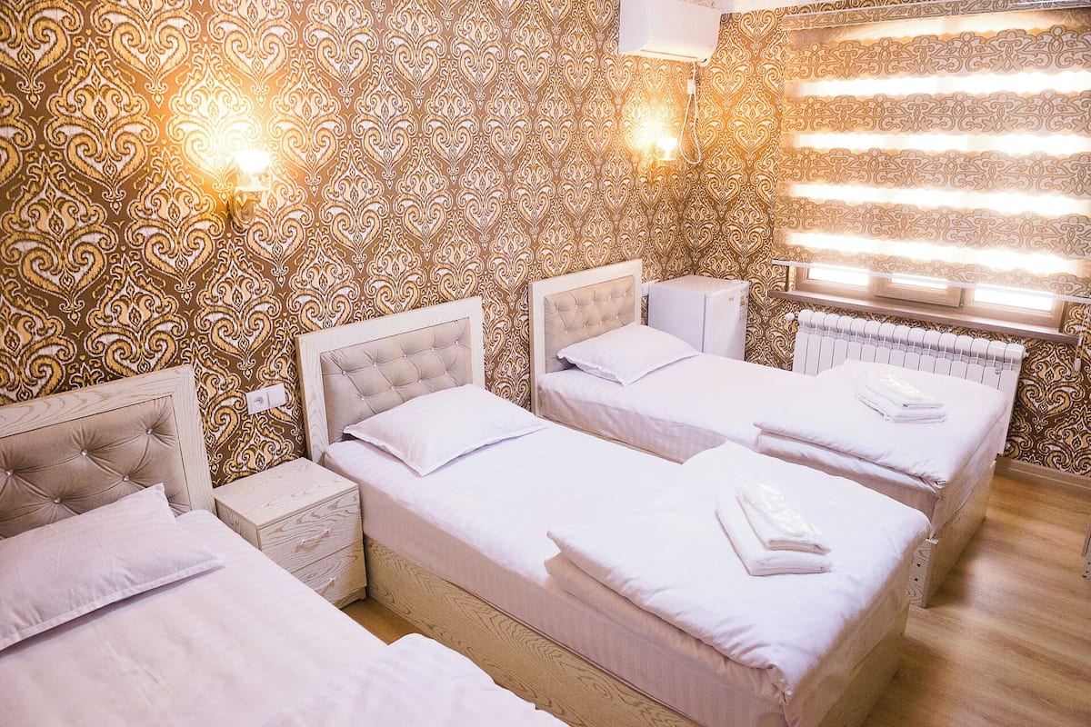 A hotel room with three beds, each with a headboard and white bedding. There are wall-mounted lights and a radiator.