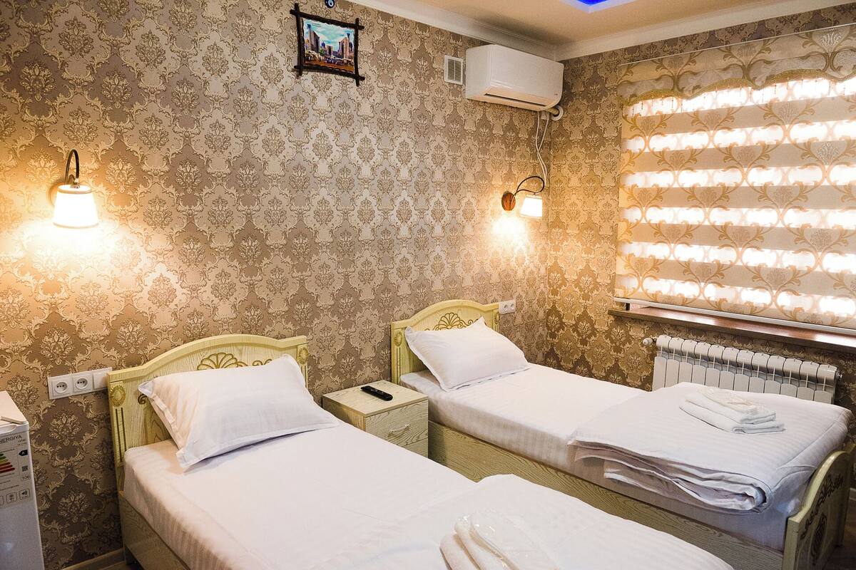 A hotel room with two single beds, a radiator, an air conditioning unit, and patterned wallpaper.