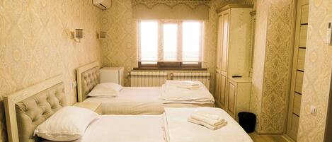 A hotel room with two beds, a radiator, a window with curtains, and patterned wallpaper.