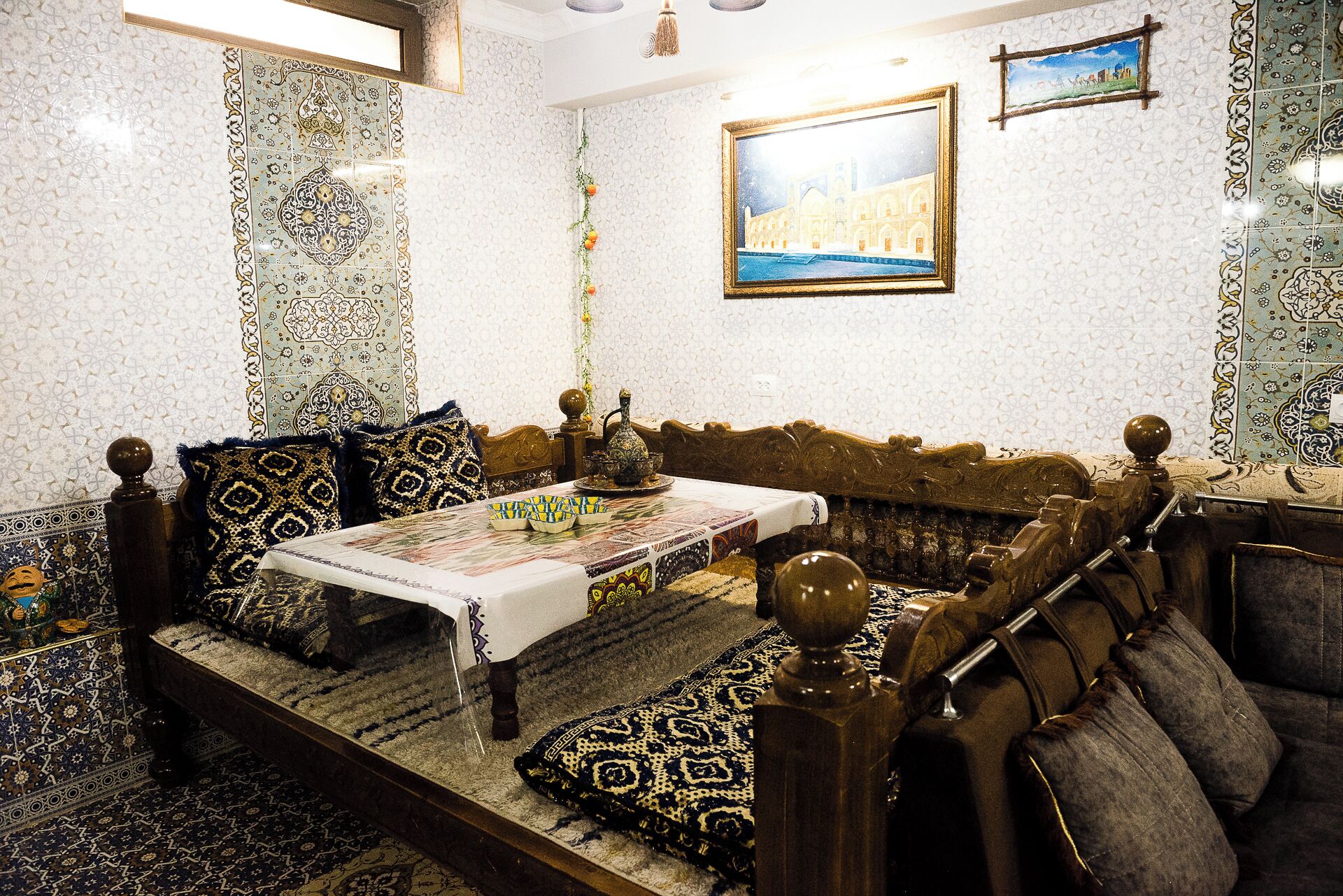 Une pièce de style marocain traditionnel, avec des carreaux décoratifs, un canapé, une table sur laquelle est disposé un service à thé, et un tableau encadré accroché au mur.