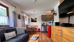 A modern living room with a sofa, a coffee table, and a kitchen area with wooden cabinets and a TV. - Fewo Sonnenglück - dreamlike 2-room apartment for 1-2 persons with corner balcony (Schönau am Königssee)