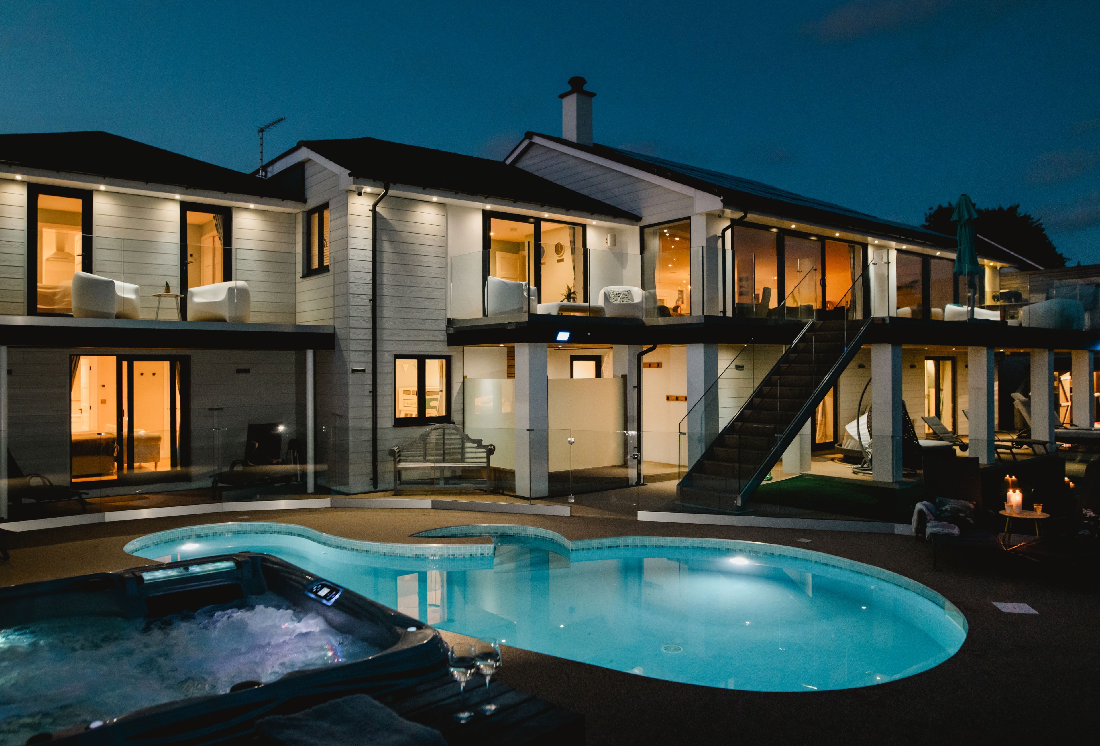 A modern two-story house with a swimming pool, outdoor seating, and a staircase leading to the upper floor.