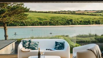 A modern outdoor seating area with a white sofa and armchair, a bottle of wine, and a glass of wine on a wooden table.