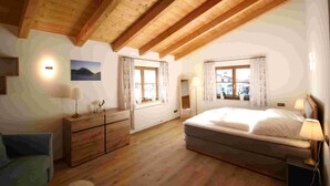 Une chambre avec un plafond en bois, un lit, une commode, une lampe et une fenêtre avec des rideaux.