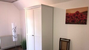 A room with a white wardrobe, a wooden chair, a radiator, and a painting on the wall. - Holiday Home 'Am Fulda Ufer' with Wi-Fi (Rotenburg an der Fulda)