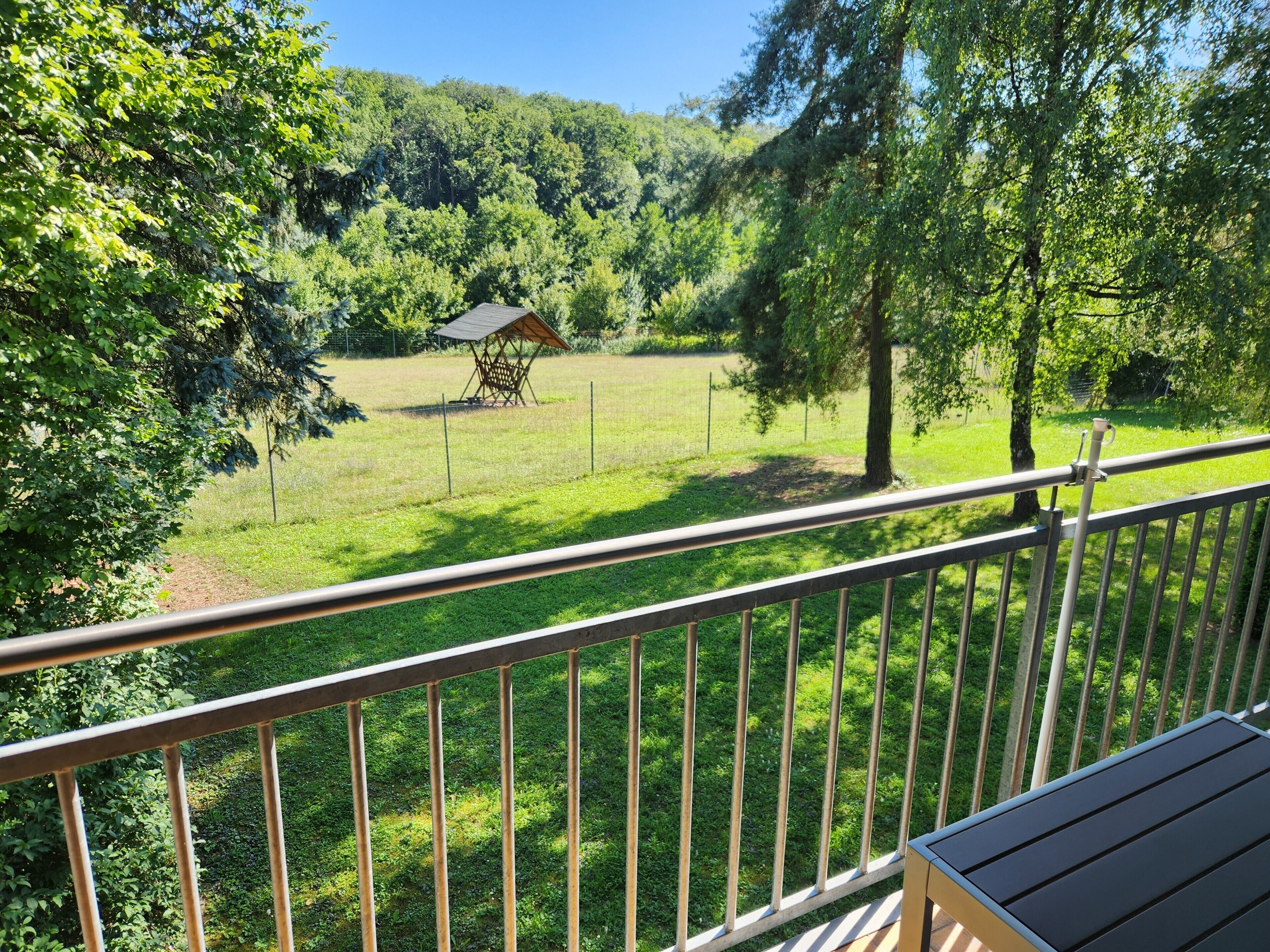 Un balcon donnant sur un espace verdoyant, avec une terrasse en bois et une rambarde en métal.