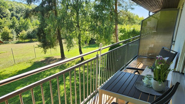 A balcony with a table and chairs, overlooking a grassy area and trees. - Holiday Apartment 'Bacchus' with Private Balcony, Shared Terrace (Iphofen)