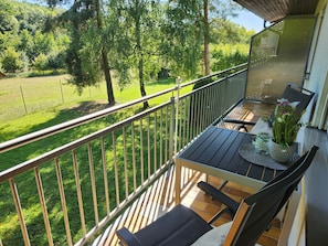 Un balcón con mesa y sillas, con vista a un área verde y árboles.