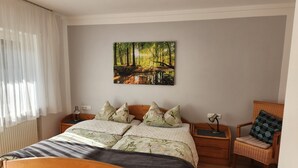 A bedroom with a wooden bed, a wall-mounted painting of a forest, a chair, and a nightstand with a lamp. - Holiday Apartment 'Bacchus' with Private Balcony, Shared Terrace (Iphofen)