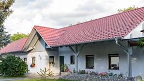 A two-story house with a red-tiled roof, white walls, and a stone wall with plants. - Holiday flat ‘Silvaner’ with private balcony, shared terrace and communal garden (Iphofen)