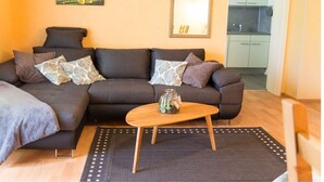 A living room with a sofa, a coffee table, a rug, a painting, and a mirror. - Holiday flat ‘Silvaner’ with private balcony, shared terrace and communal garden (Iphofen)
