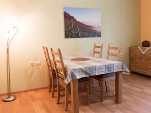 Uma sala de jantar com mesa posta para quatro pessoas, cadeiras de madeira, abajur e quadro pendurado na parede.