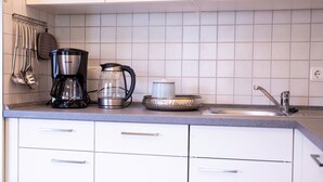 Een keuken met witte kastjes, een koffiezetapparaat, een waterkoker en een spoelbak.