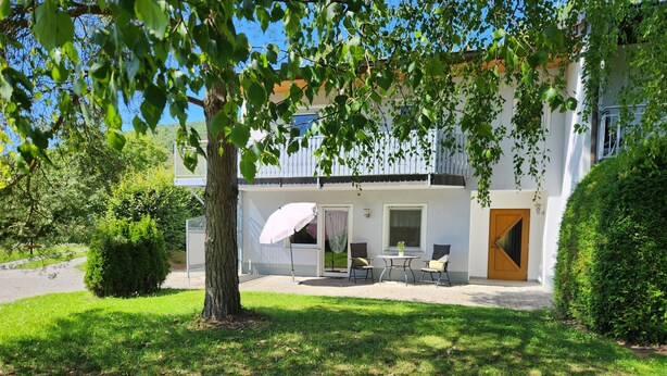 Een gebouw met twee verdiepingen, een overdekt terras, een boom en een verzorgd gazon.