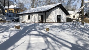 A snow-covered building with a sloped roof, a front door, and windows.