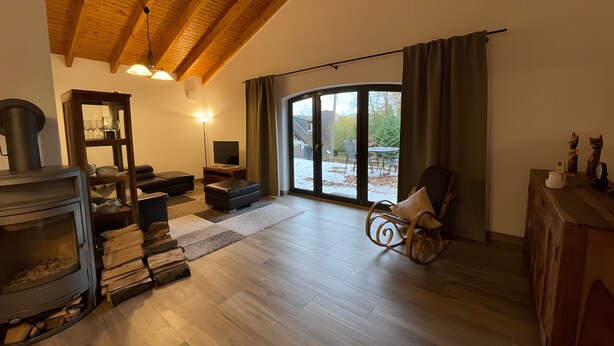 Een woonkamer met een open haard, een bank, een stoel en uitzicht door een glazen deur op een buitengebied.