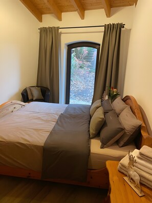 A bedroom with a bed, a chair, a window with curtains, and a view of the outdoors.