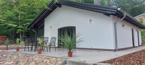 A modern building with a white exterior, a black roof, and a covered patio area with outdoor seating and potted plants.