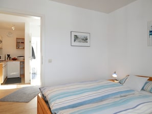 Ein Schlafzimmer mit Bett, Nachttischlampe und einer Tür, die in eine Küche führt.