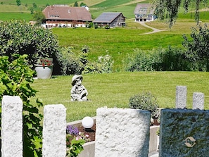 Ländliche Landschaft mit einer Steinstatue, einem Steinzaun und einem Haus im Hintergrund.