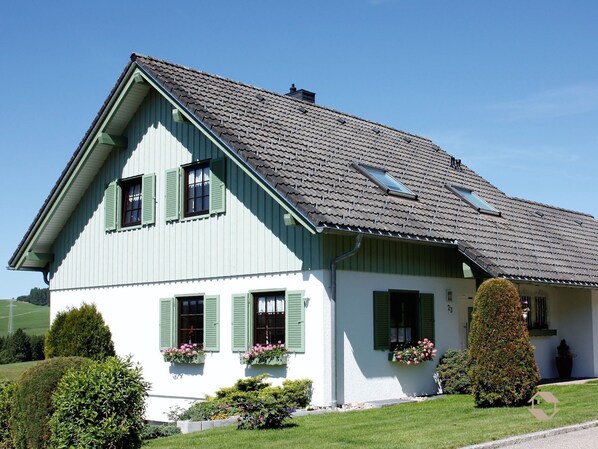 Ein zweistöckiges Haus mit einem steilen Satteldach, Dachgauben und grünen Fensterläden.