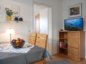 Ein Zimmer mit Esstisch, Stuhl, Fernseher, Bücherregal und einer Tür.
