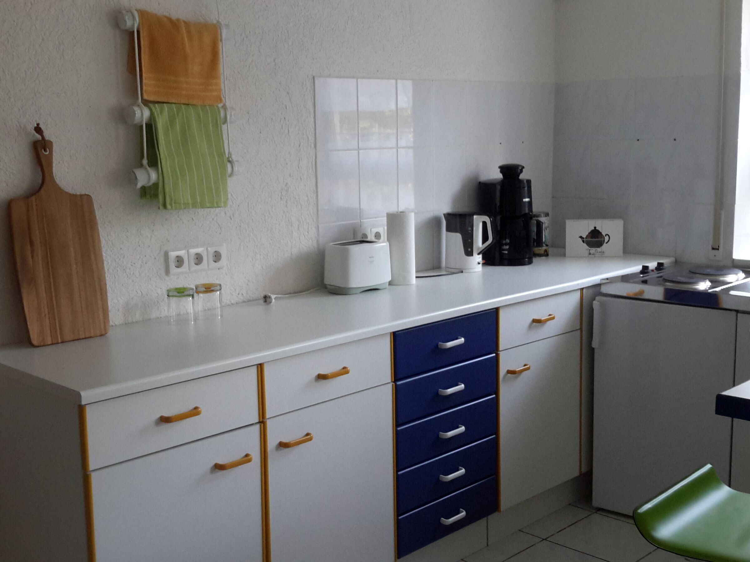 Ett kök med vita skåp, en bänkskiva, en kaffebryggare, en brödrost och en grön stol.