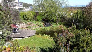 Un jardín con un estanque, plantas en macetas y una terraza de madera.