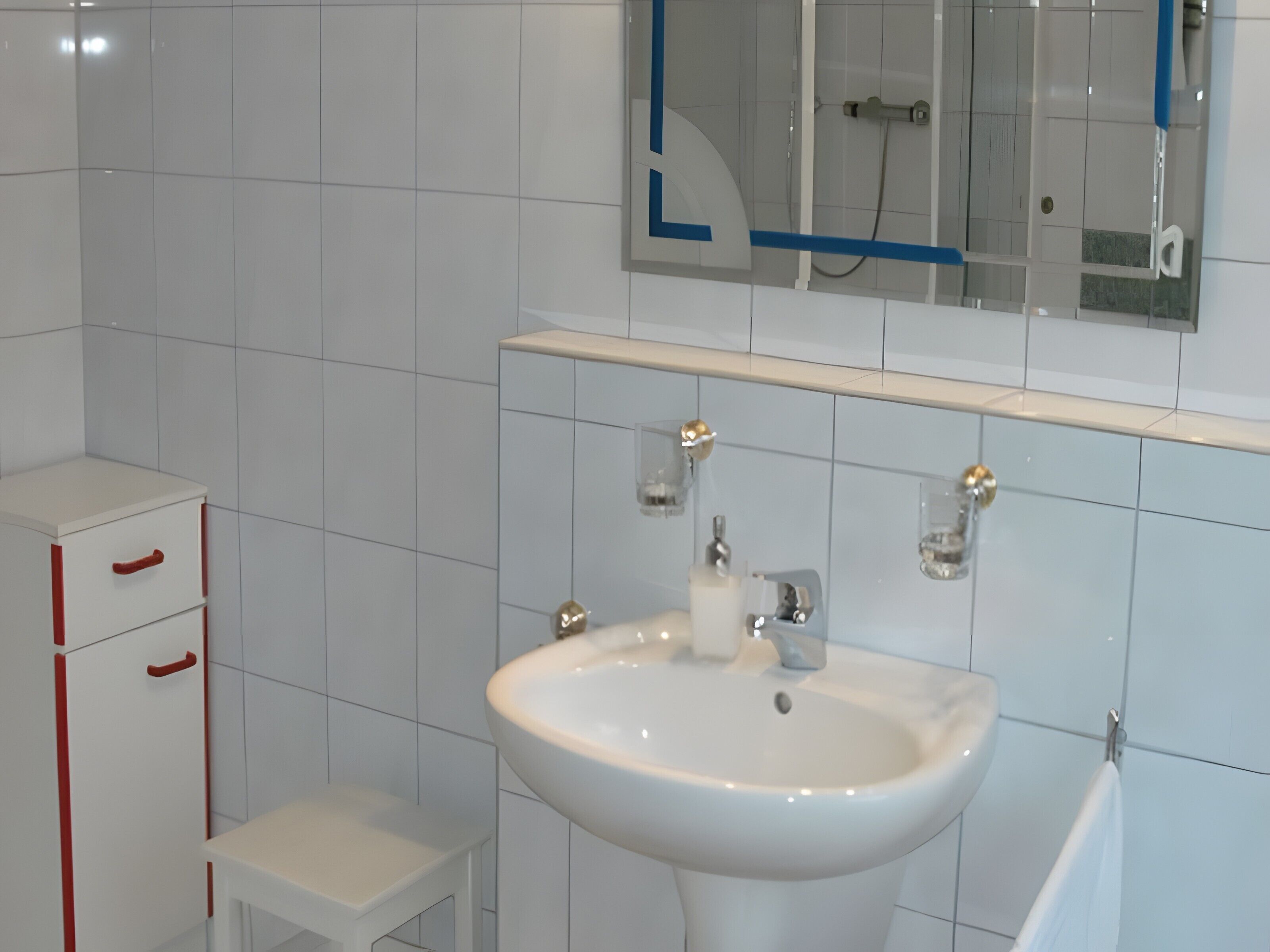 A bathroom with a white sink, a mirror, and a cabinet with red handles.