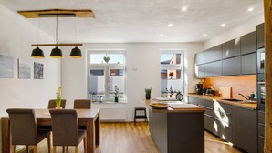 A modern kitchen with a central island, wooden flooring, pendant lighting, and a view of the outside.