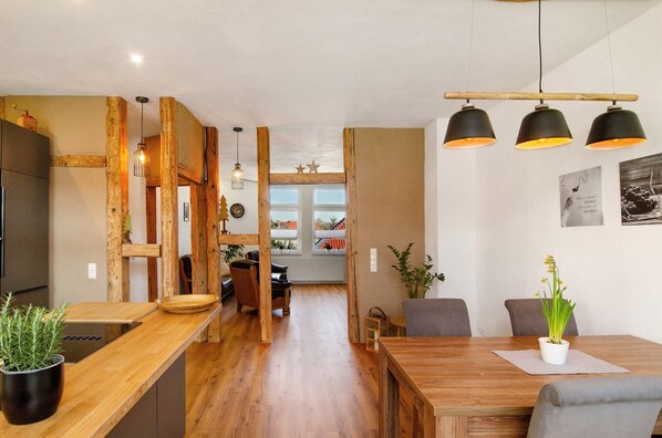 A wooden interior with a dining table, chairs, a potted plant, and a hanging light fixture.