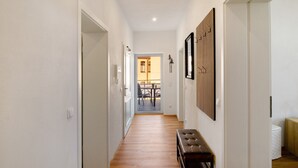 A hallway with wooden flooring, a bench, and a door leading to a room with a white toilet and a small table.