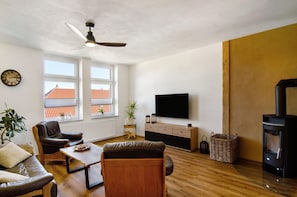 A living room with a sofa, armchair, coffee table, TV, fireplace, and a ceiling fan.