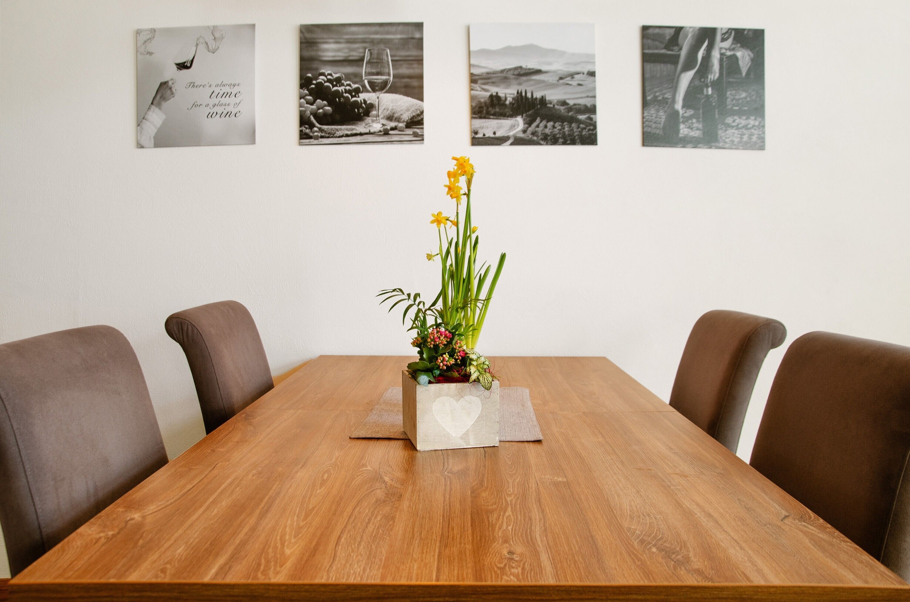 Una mesa de conferencias con un centro de mesa floral, cuatro sillas marrones y tres cuadros en la pared.