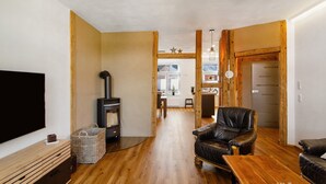 A living room with a fireplace, wooden flooring, a leather armchair, a TV, and a ceiling fan.