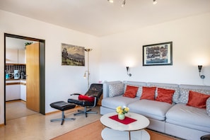 Ein Wohnzimmer mit einer Couch, einem Couchtisch, einem Sessel, einer Lampe und einem Gemälde an der Wand.