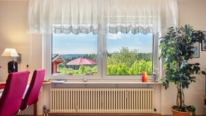 A room with a large window, a radiator, a desk with a chair, and a potted plant. - Roodbach Apartment: Mountain View, Private Terrace, Garden, Table Tennis & Wi-Fi (Lenzkirch)