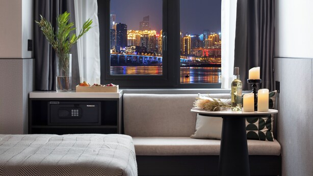 A hotel room with a bed, a sofa, a small table with candles, a bottle, and a vase with plants.