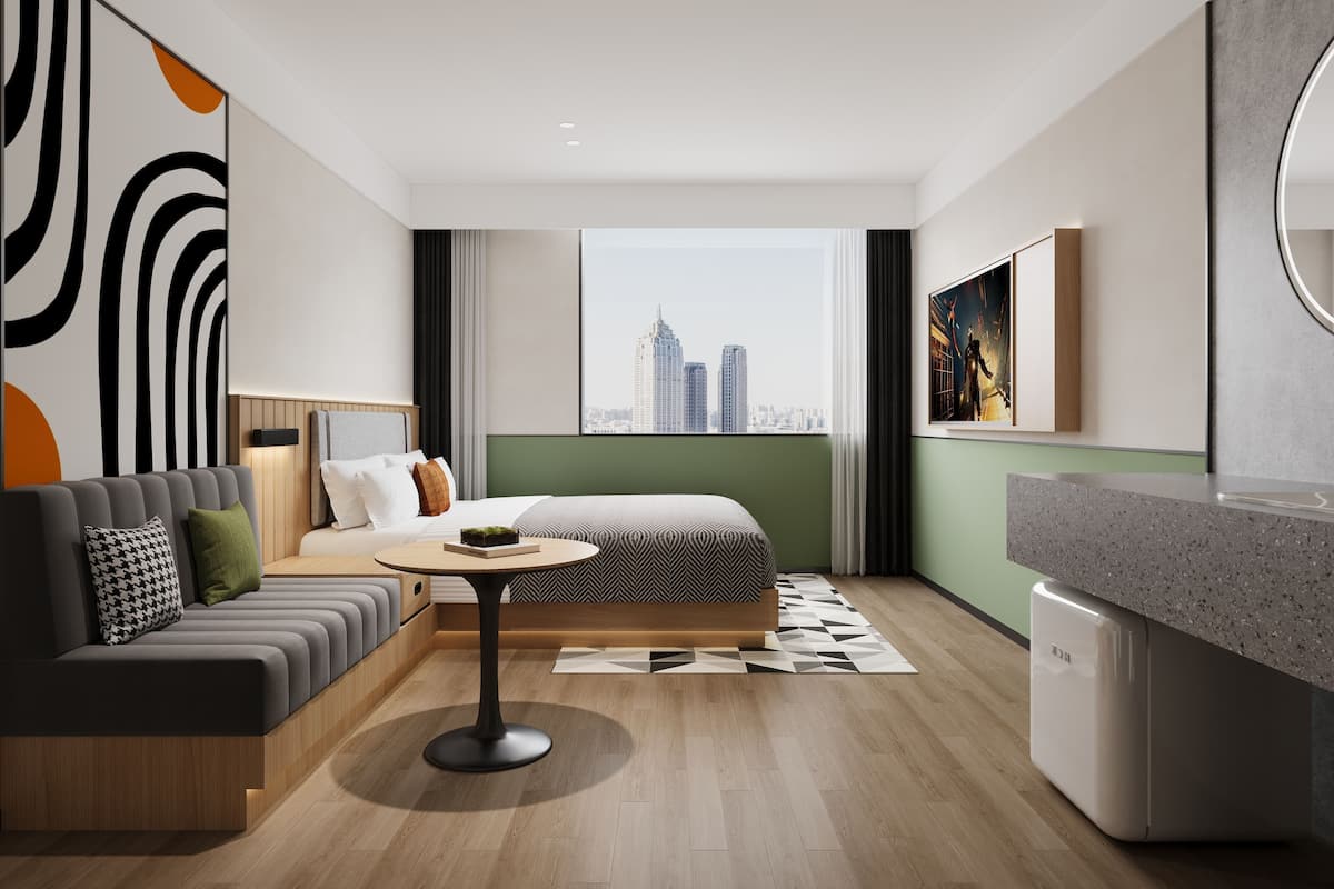A modern hotel room with a sofa, a round table, a bed, a view of the city, and a kitchen area.