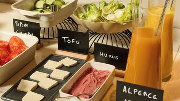 Un buffet proposant une variété de plats, chacun étant clairement identifié, comprenant des concombres, de la laitue, des tomates, du tofu, du houmous et une boisson.