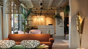 En moderne hotellobby med reception, sofa, mønstrede stole og en høj gulvlampe.