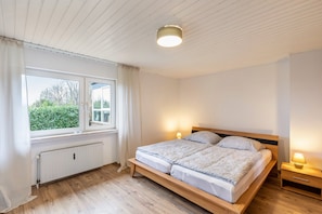 Un dormitorio con cama de madera, lámparas de noche, una ventana con cortinas y un radiador.