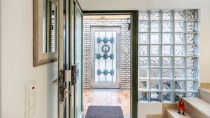 A hallway with a glass door, a brick wall, and a window with a grid pattern.