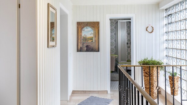A hallway with white paneling, a framed painting, a wreath, and two planters.