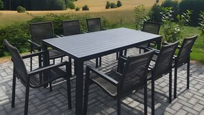 An outdoor patio with a table and chairs, a brick floor, and a view of a field and hills.