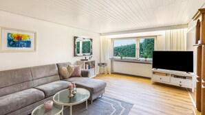 A living room with a sofa, a coffee table, a TV, a window, and a radiator.