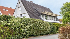 A residential house with a sloped roof, a covered porch, and a well-maintained hedge.