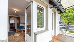 A balcony with a wooden floor, a chair, and a view of greenery.