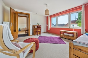 A bedroom with a bed, a chair, a desk, a window, and a door.
